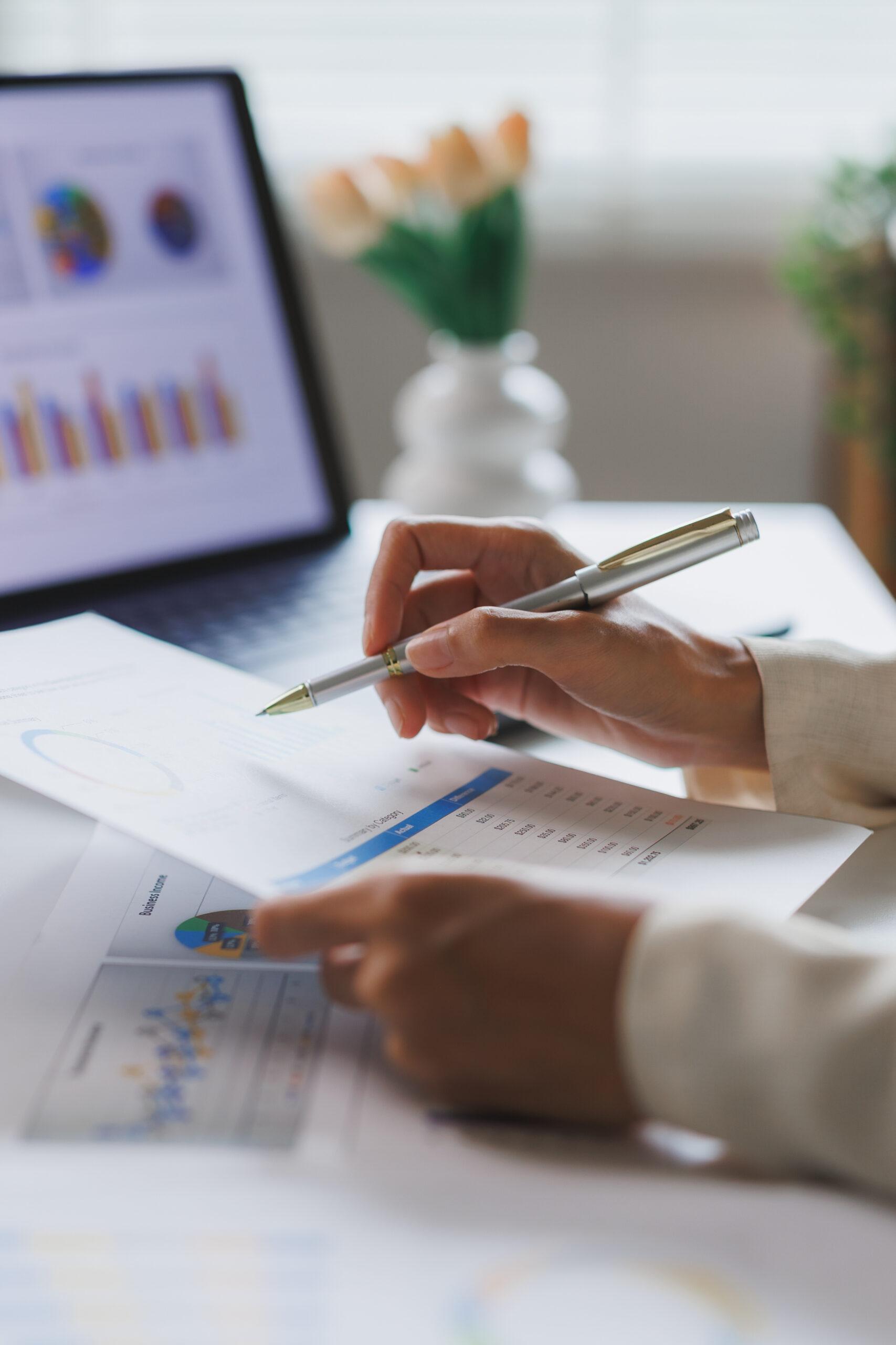 Someone reviewing a paper with figures on it, with a computer in the background
